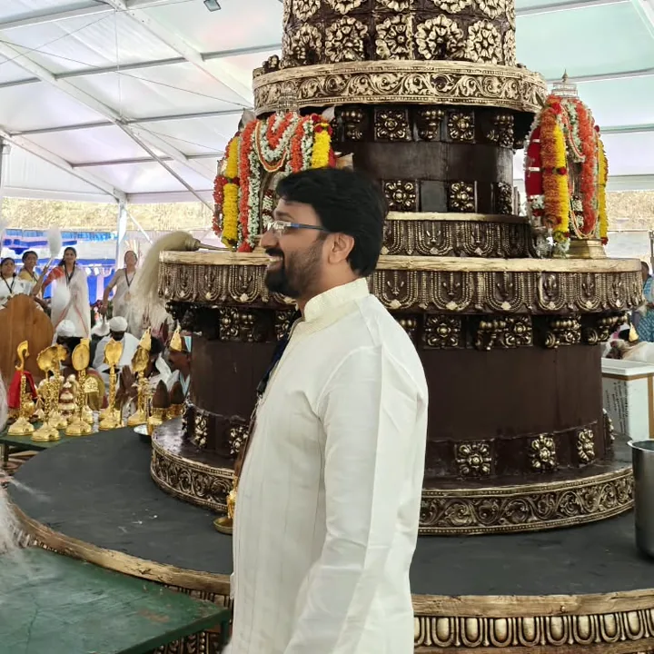 Pavan in a white kurta beside a tall decorated festival structure